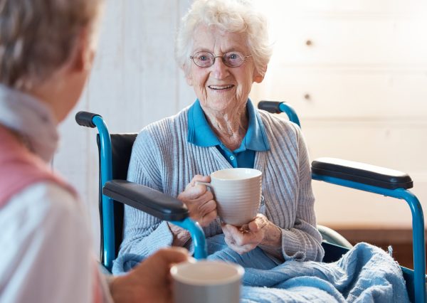 senior-wheelchair-woman-patient-with-morning-coffee-consulting-medical-conversation-mobility-disability-healthcare-retirement-nursing-home-female-happy-talking-caregiver-nurse-scaled.jpg